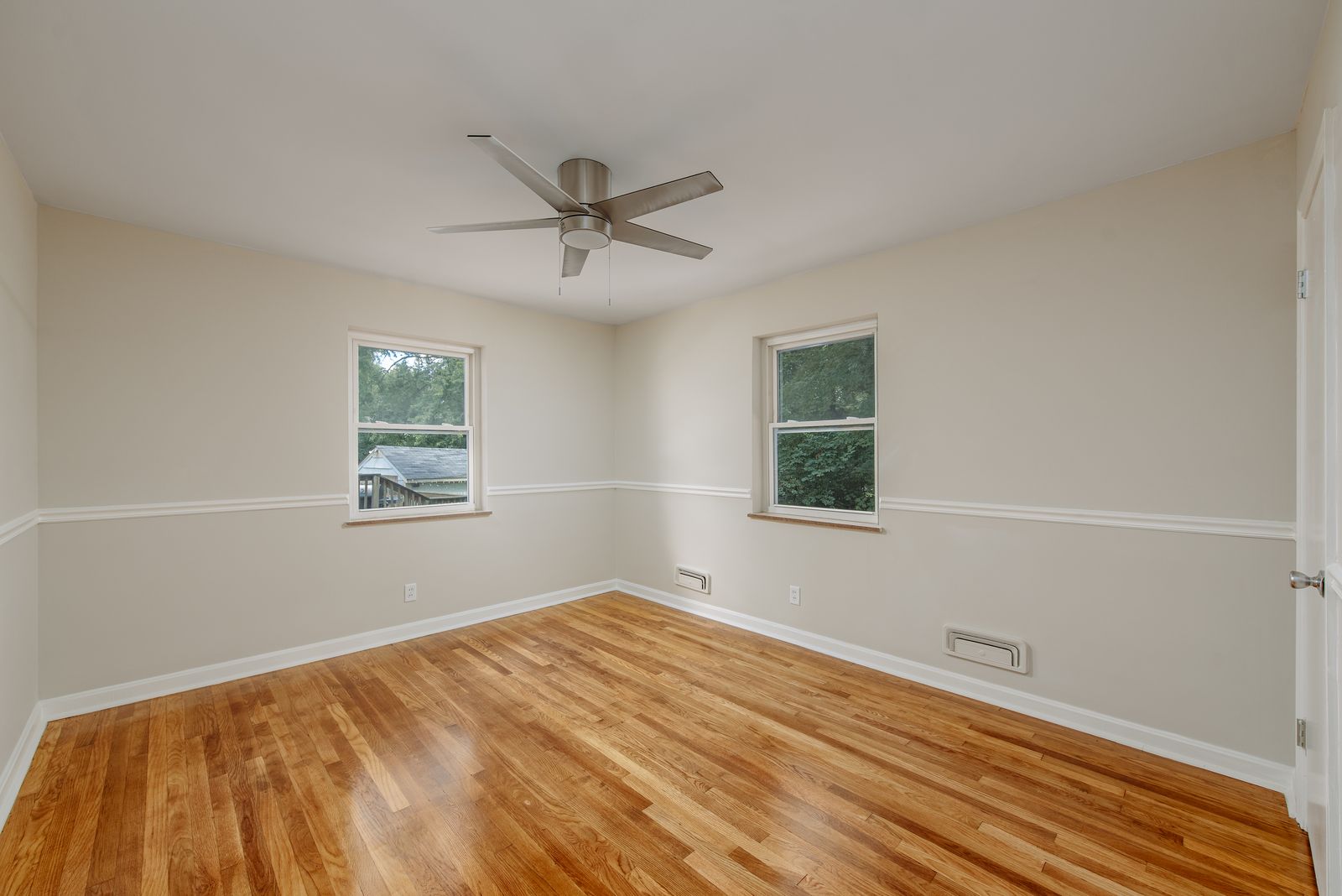 Second main-floor bedroom with chair rail molding, refinished oak floors, and a ceiling fan