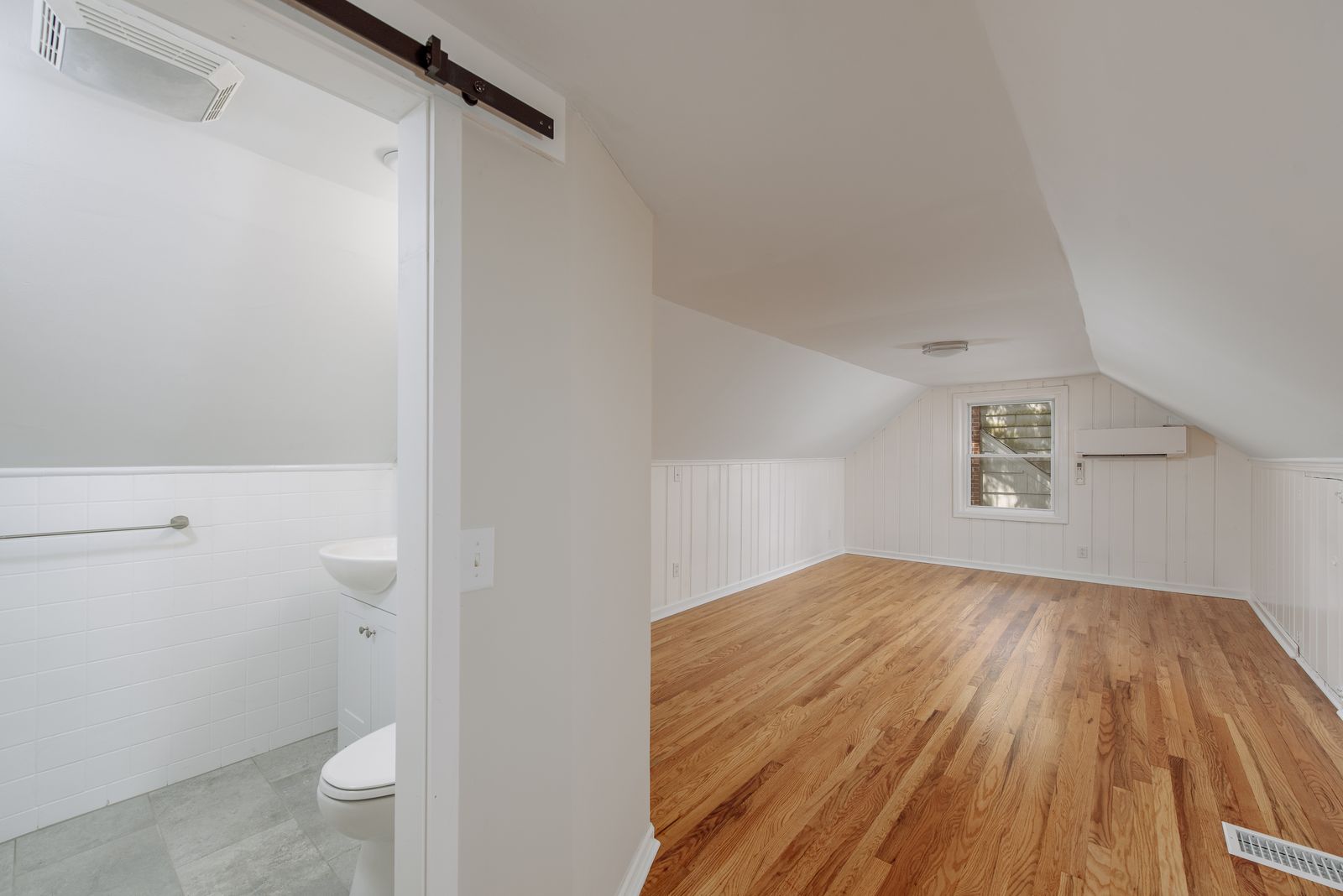 Upstairs bedroom suite with vaulted sloped ceilings, refinished hardwood floors, paneled walls, and an adjoining half bath