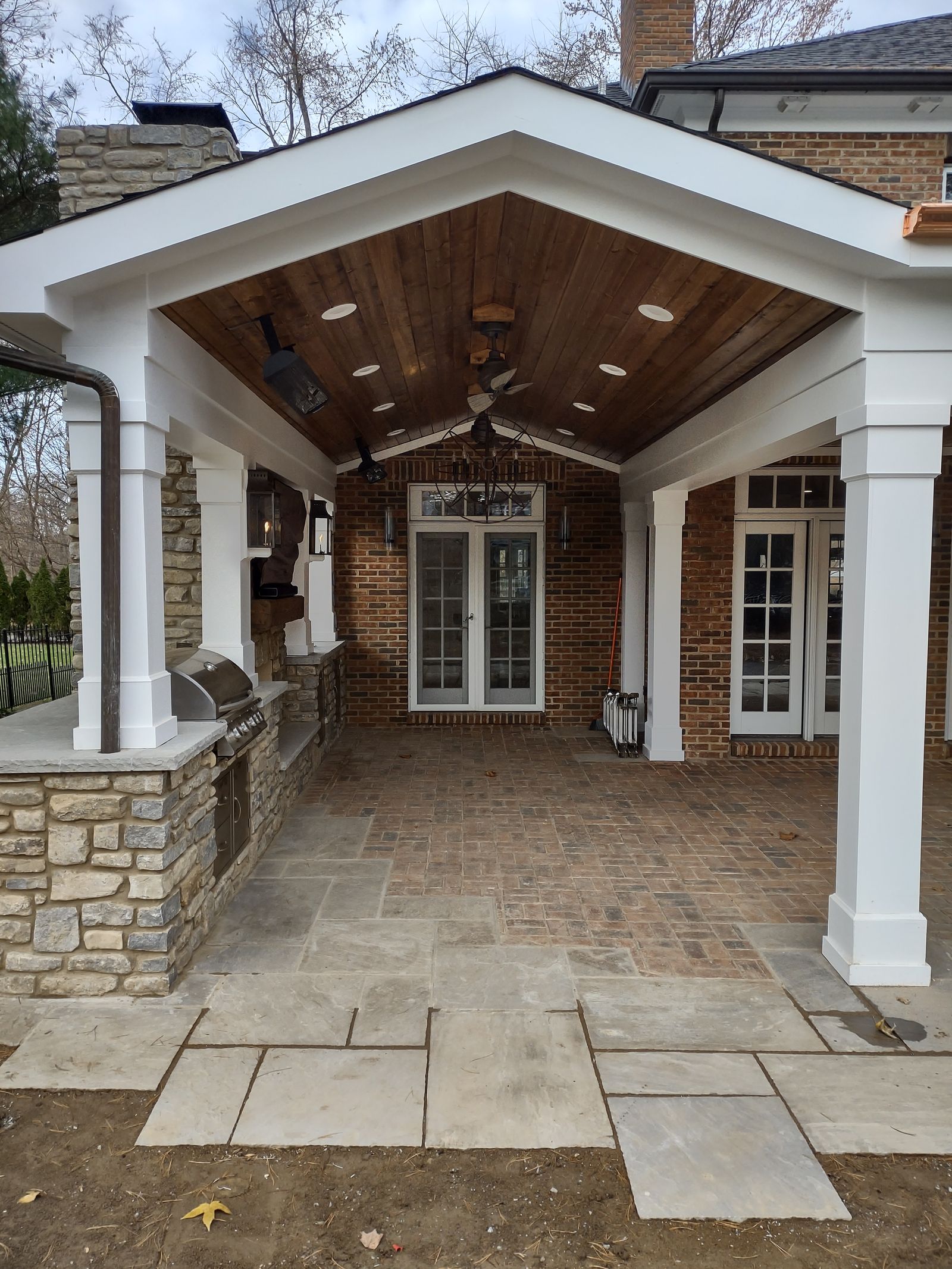 Gable-roofed porch with stone-based columns and built-in grill beside the brick home