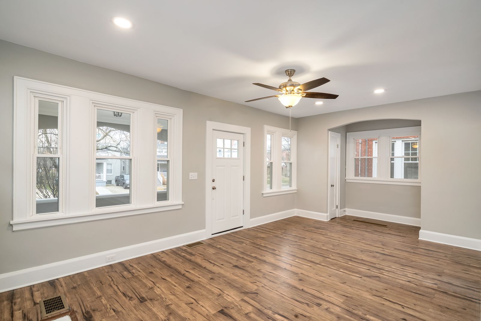 Living room with a new white front door, large front windows, and an arched nook, finished in soft gray paint and new flooring