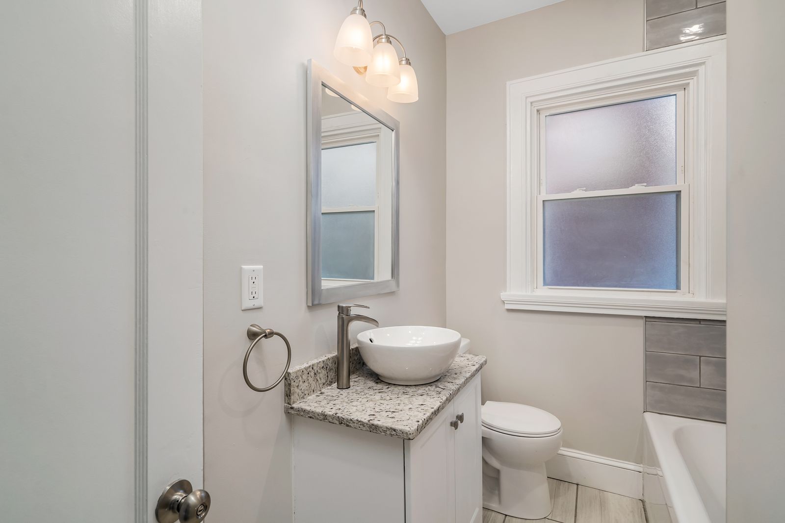 Renovated hall bathroom with a vessel-sink vanity, granite-look counter, framed mirror, and new fixtures