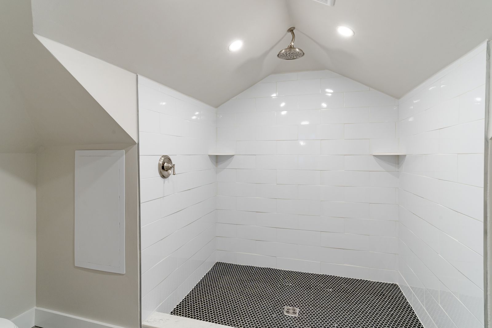 Attic walk-in shower with white subway tile, corner shelves, and a black penny-round tile floor