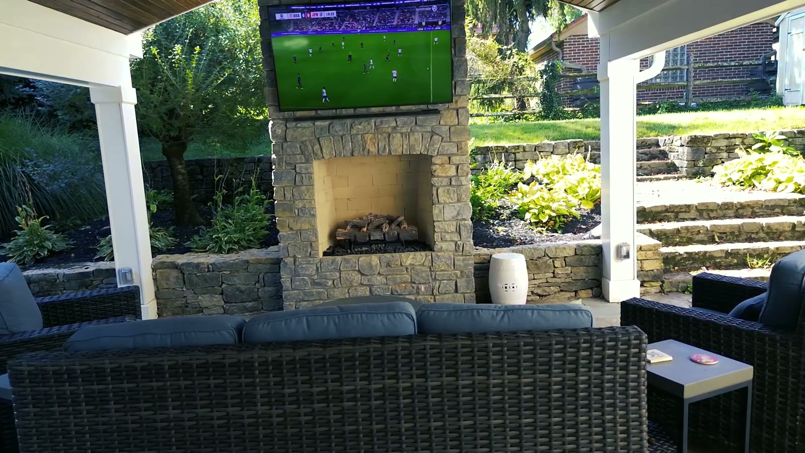 A covered patio with stone fireplace and lounge seating, set to music.