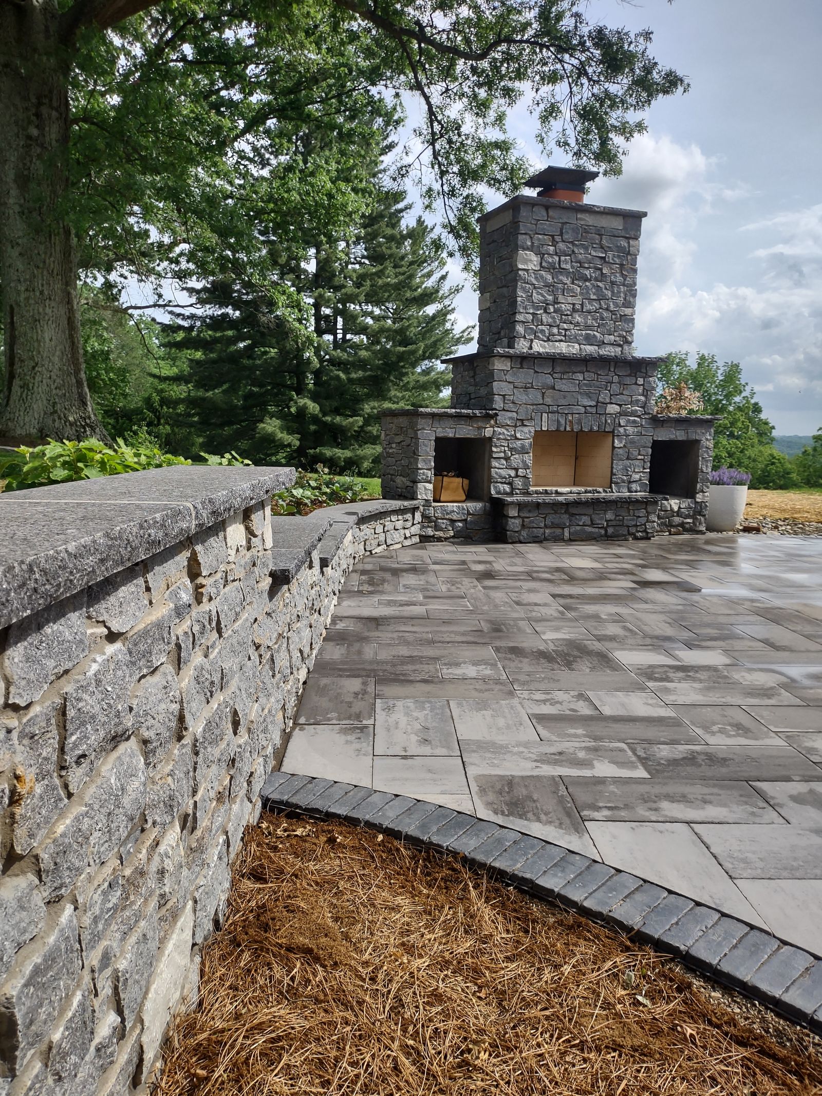 Stone fireplace viewed from paver patio with curved stone seat wall