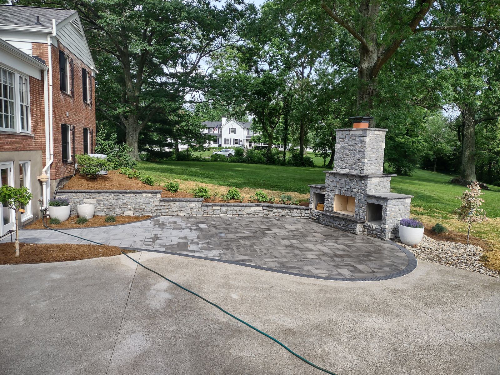 Backyard paver patio and stone fireplace alongside a brick home