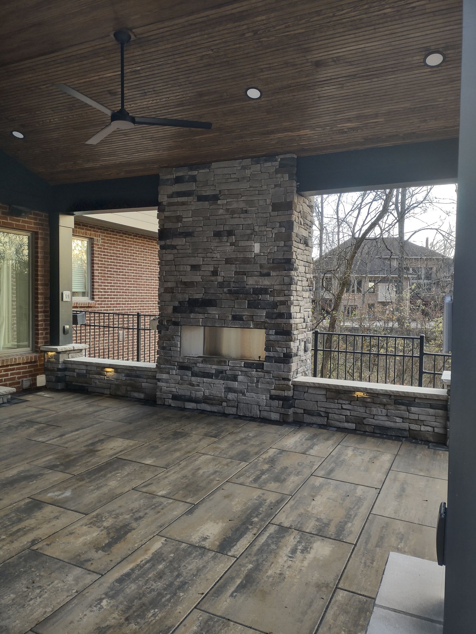 Covered porch interior with stone fireplace, TV niche, and ceiling fan
