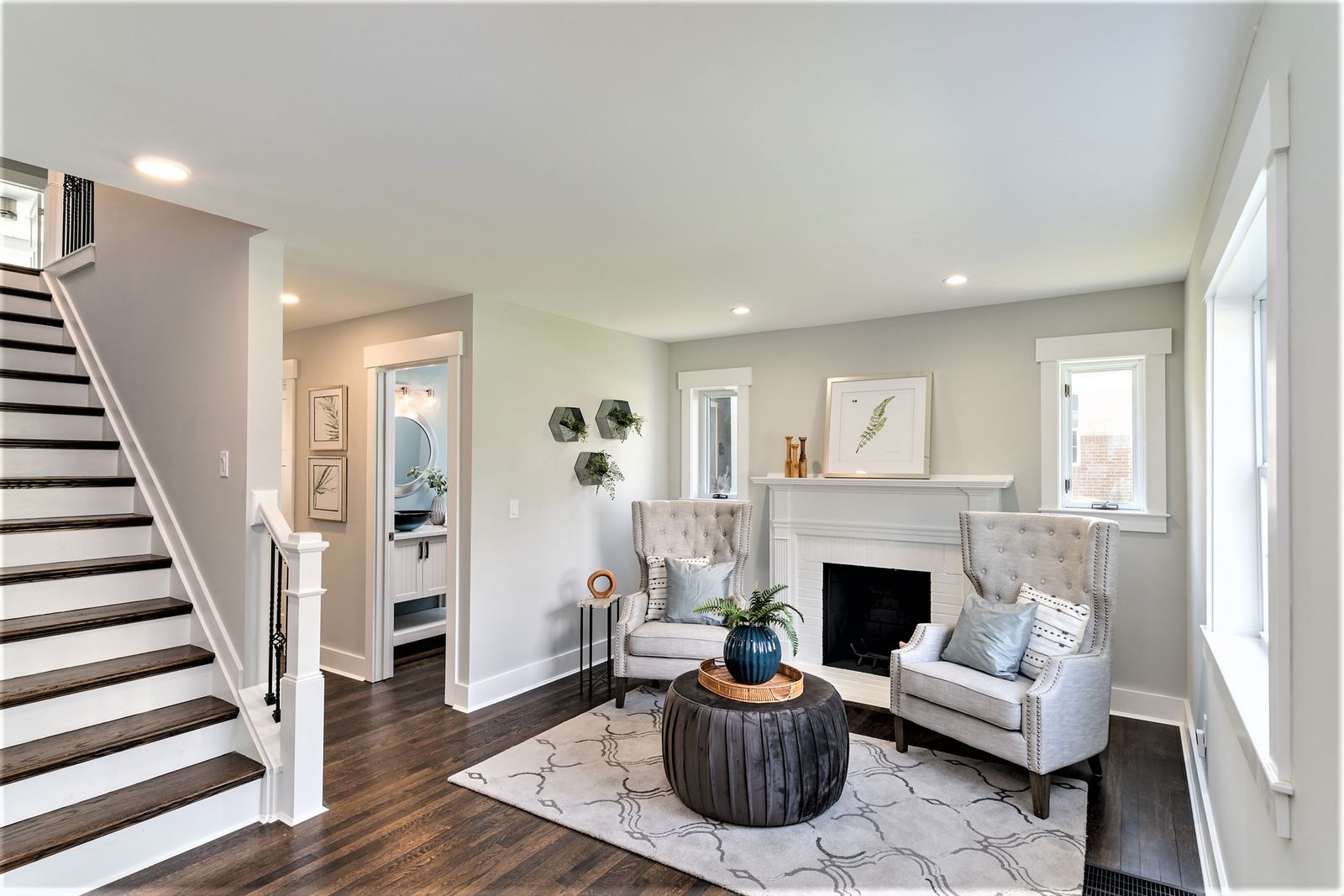 Bright living room with white fireplace surround, dark hardwood floors, and a staircase with white railings