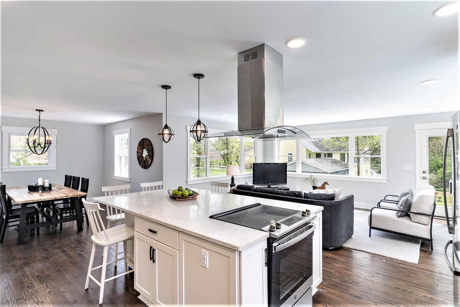Open kitchen with large white island, cooktop, stainless hood, and a view into the living area