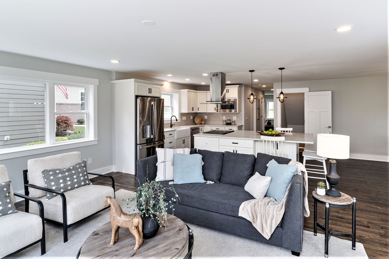 Open-concept living room with navy sofa and armchairs looking into the white kitchen