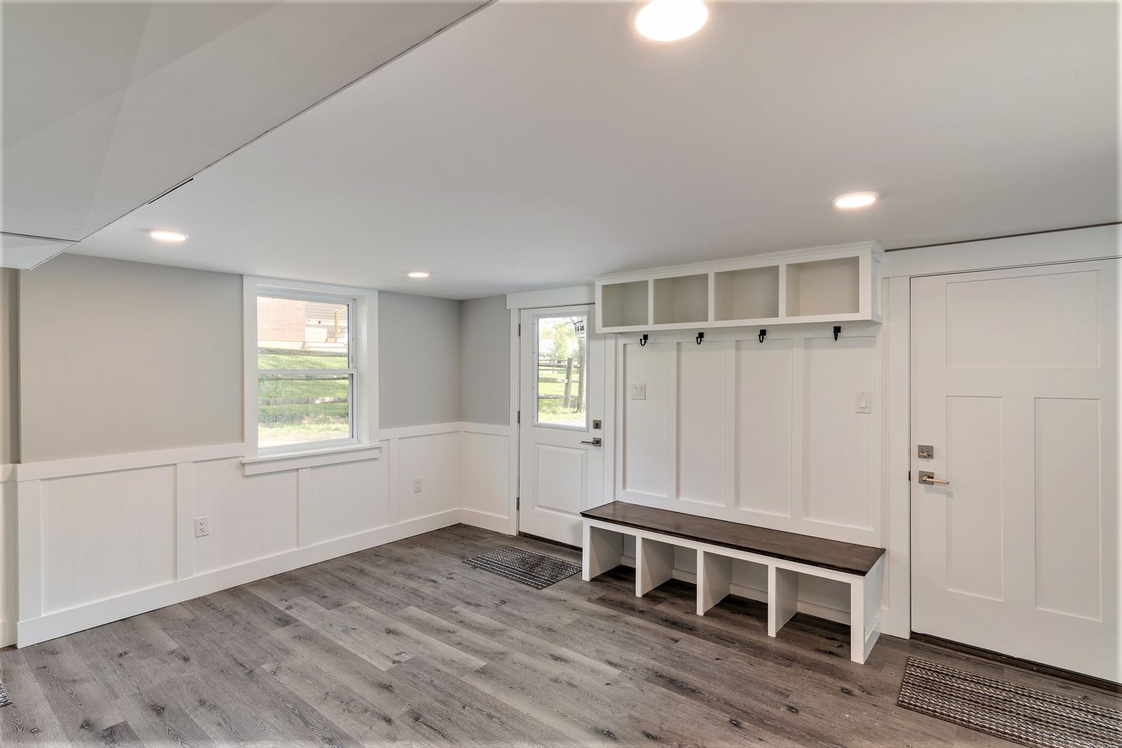 Mudroom with white built-in lockers, bench, wainscoting, and plank flooring