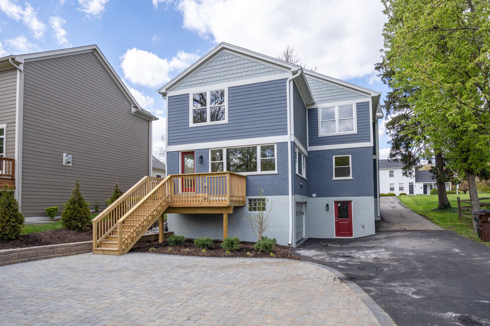 Renovated rear from the driveway side with new deck stairs, blue siding, and red walk-out door