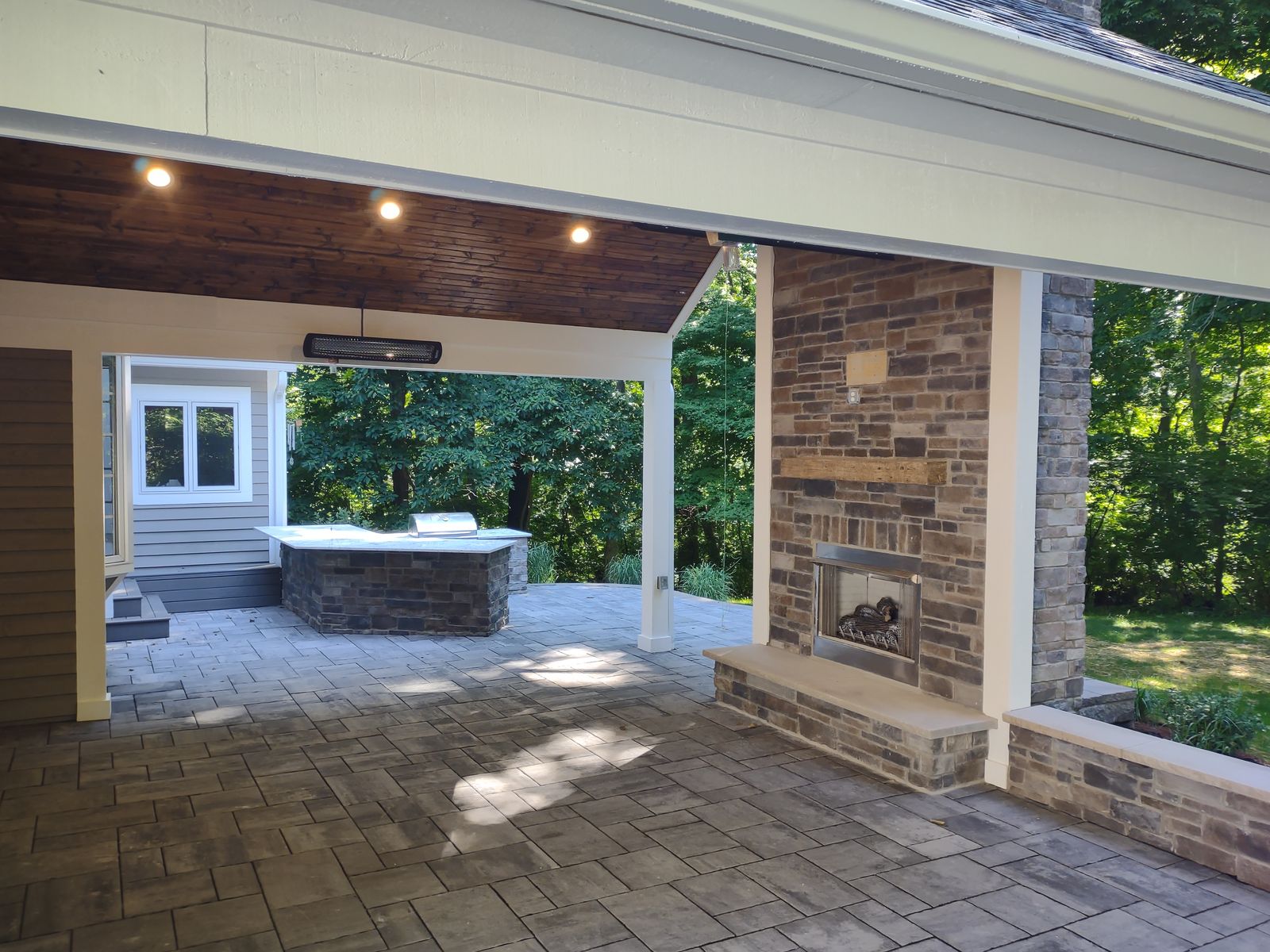 Covered porch interior with stone fireplace, ceiling heater, and an outdoor grill island beyond