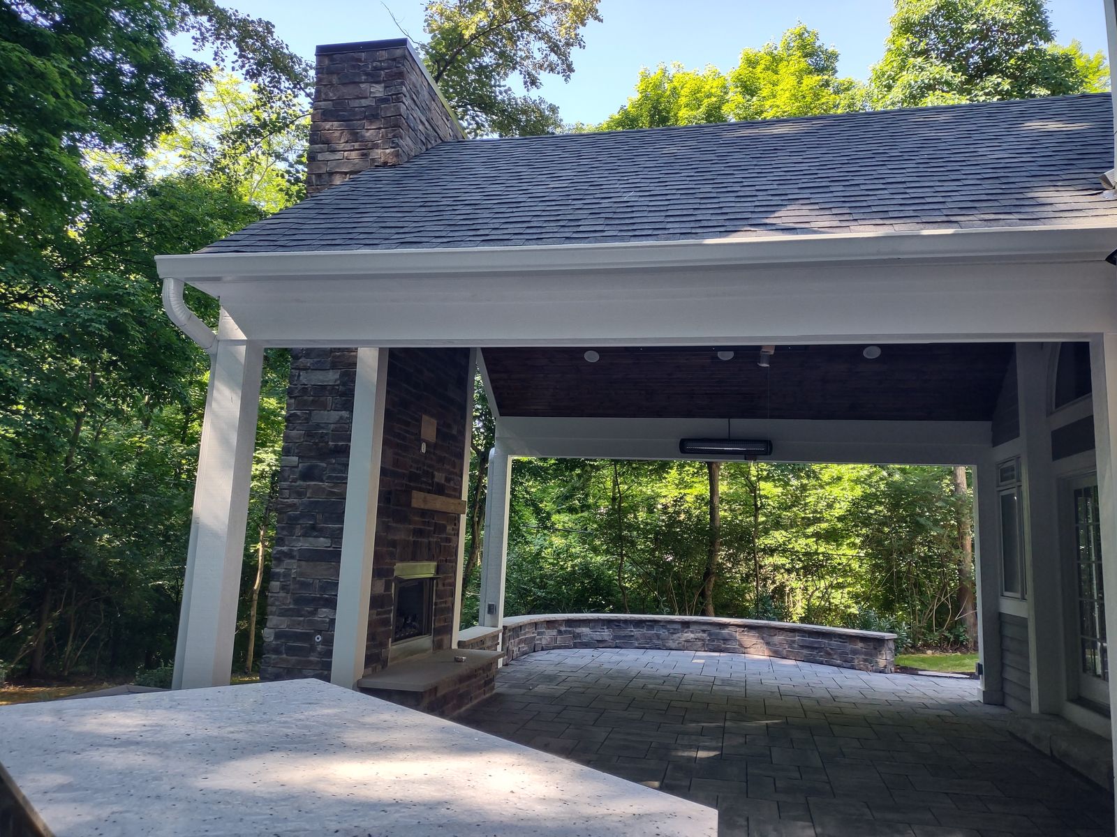 Covered porch with hot tub and stone half wall overlooking wooded yard